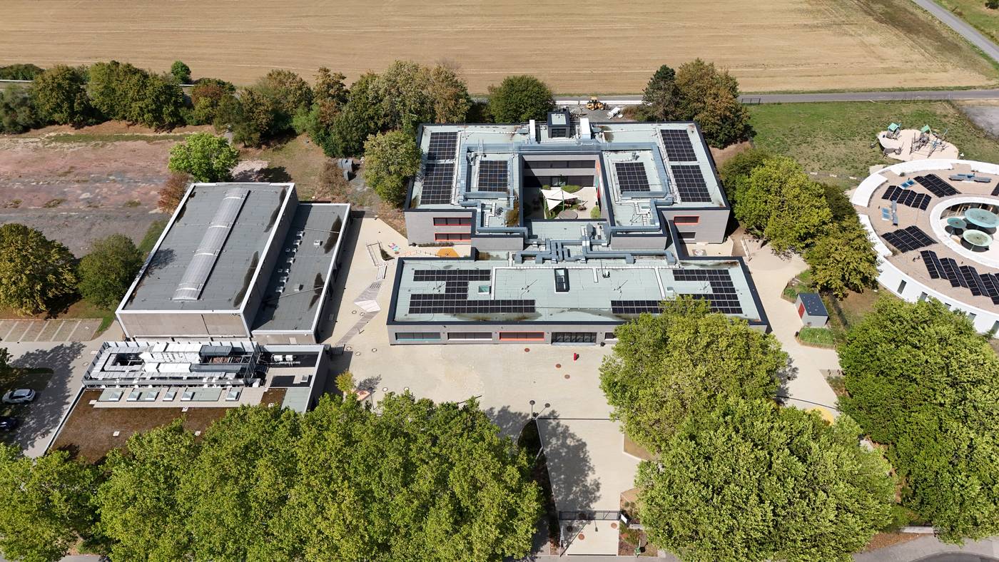 Das Schulgel&auml;nde schr&auml;g von oben: die flachen Geb&auml;uderiegel, der Schulhof und ringsum B&auml;ume und abgeerntete Felder