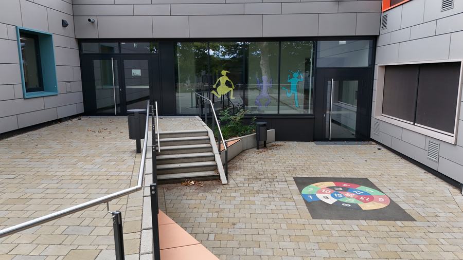 Ein Innenhof mit Glast&uuml;ren, einer Treppe mit Gel&auml;nder und einem runden, bunt aufgemalten Spiel auf dem Pflaster
