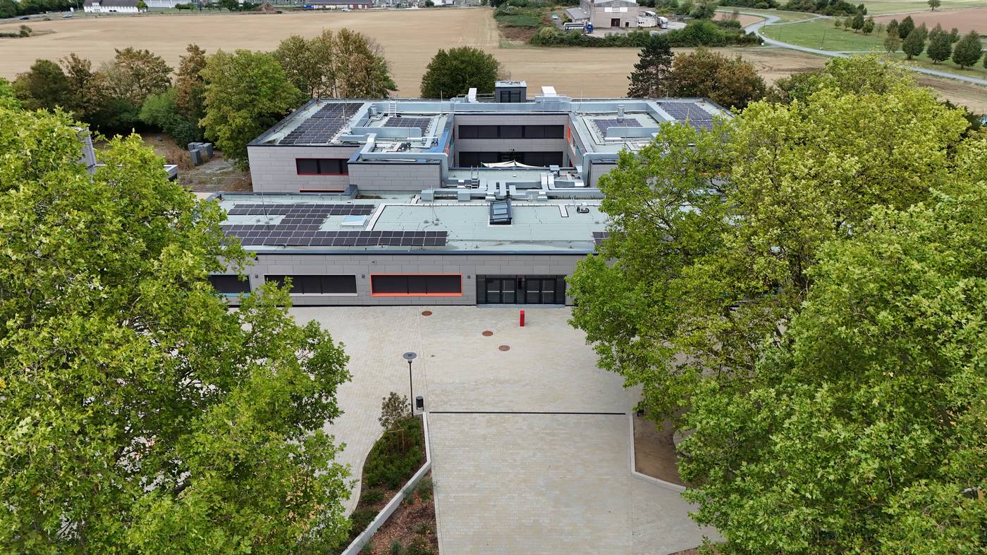 Die Schule von vorn, links und rechts von hohen B&auml;umen ges&auml;umt