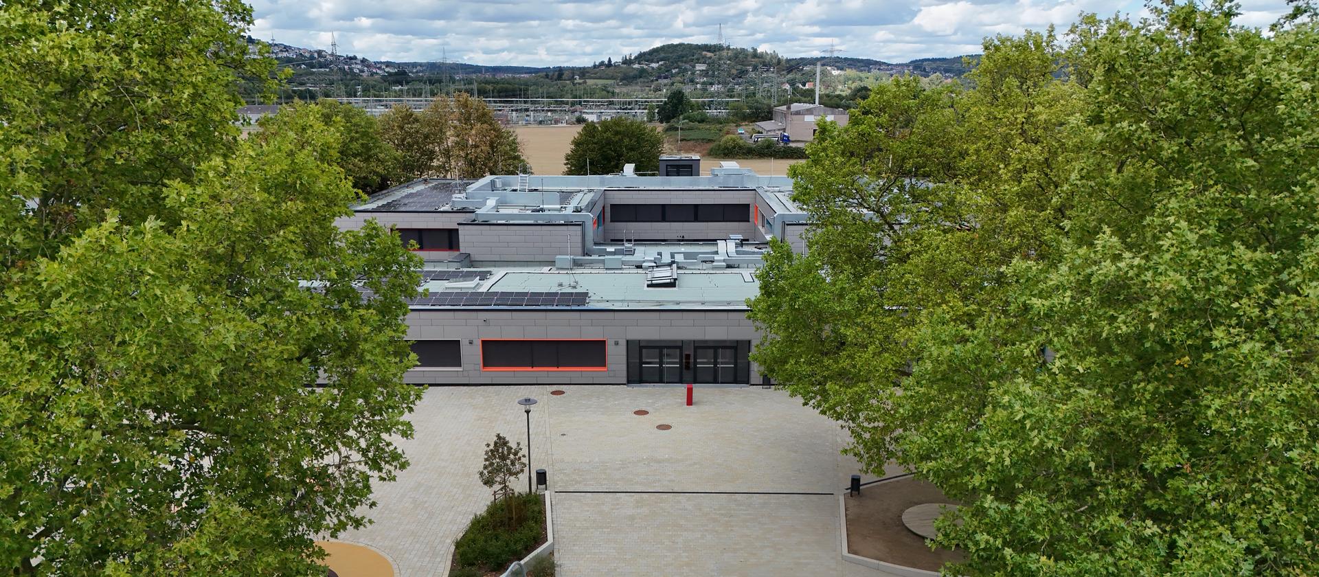 Die Grundschule Gie&szlig;en-West von vorn, zwischen zwei Baumreihen, dahinter Felder und H&uuml;gel